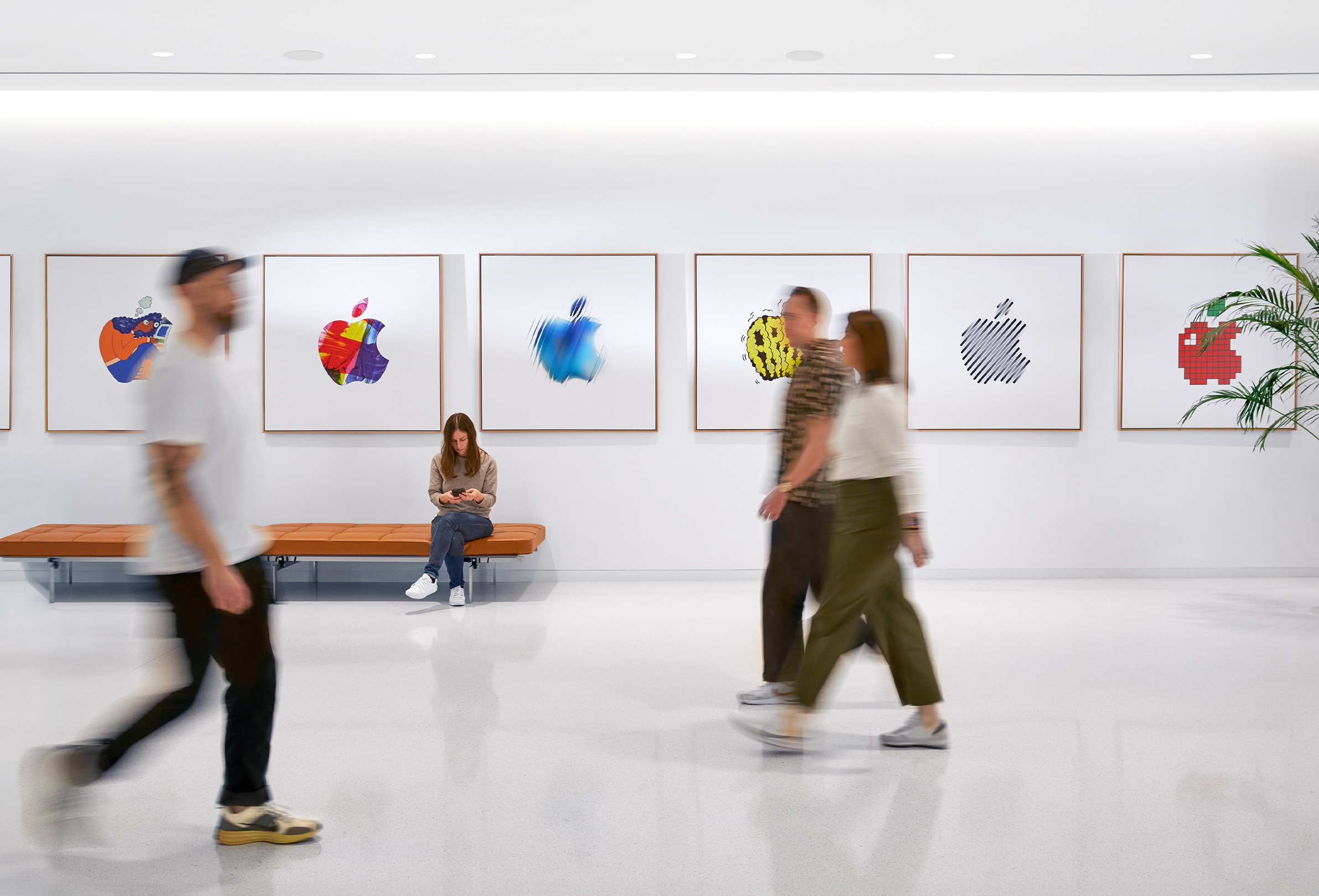 三位 Apple 同事走過佈滿彩色 Apple 標誌的內牆，第四位員工則坐在長椅上。