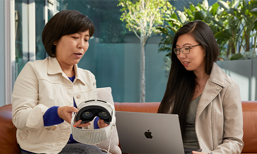 Jessica 在室內使用 MacBook，身後有道打開通向庭院的門。她坐在一位 Apple 同事旁邊，對方正在向她展示 Apple Vision Pro。