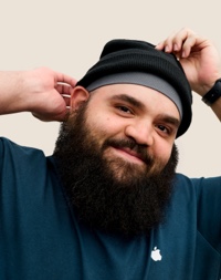 Portret van een glimlachende Apple Retail-medewerker met een volle baard en een muts op.