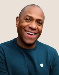 Portret van een lachende Apple Retail-medewerker met kort donkergrijs haar.