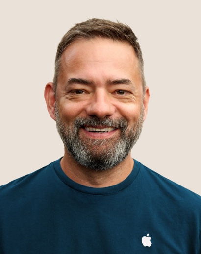 Portret van een lachende Apple Retail-medewerker met kort grijs haar en een baard.