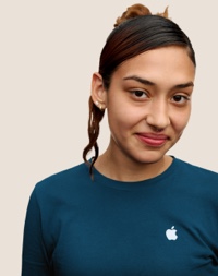 Portret van een glimlachende Apple Retail-medewerker met lang donker haar met roze highlights.