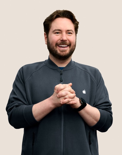 Portret van een lachende Apple Retail-medewerker met kort, golvend donker haar en een baard.