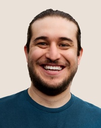 Portret van een lachende Apple Retail-medewerker met donker haar en een baard.