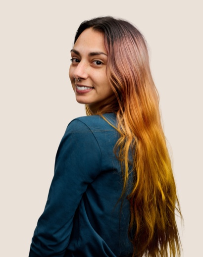 Portret van een glimlachende Apple Retail-medewerker met lang bruin haar die over haar schouder in de camera kijkt.