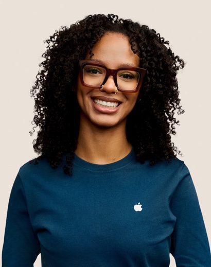 Portret van een glimlachende Apple Retail-medewerker met lange, donkere krullen en een bril.