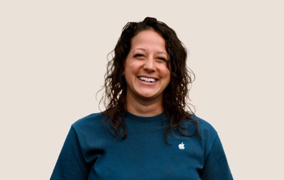 Portret van een lachende Apple Retail-medewerker met lang, donker, golvend haar.