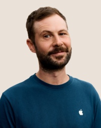 Portret van een glimlachende Apple Retail-medewerker met donker haar en een baard.