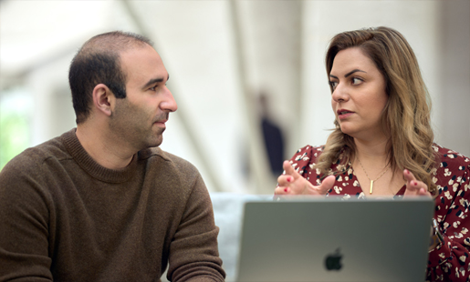 Desireh zit achter een MacBook en praat met een collega