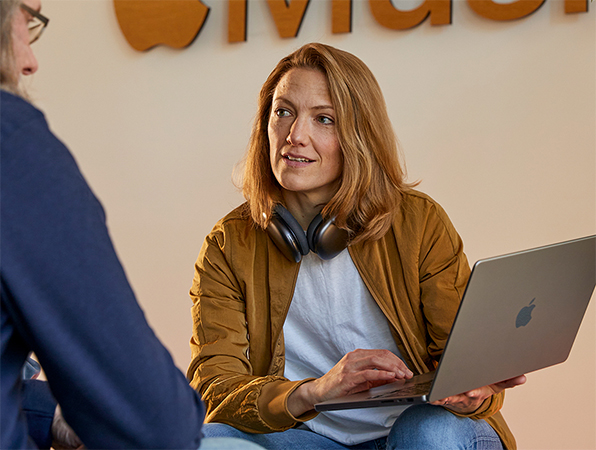 兩位 Apple 銷售及業務發展團隊成員正在對話，其中一人拿著 MacBook，坐在有 Apple Music 標誌的牆前。