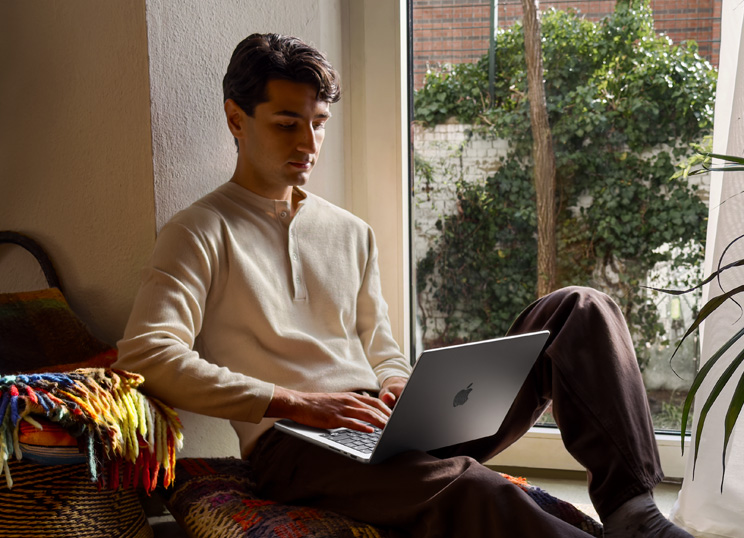 Uma pessoa sentada no chão usando um MacBook ao lado de uma janela