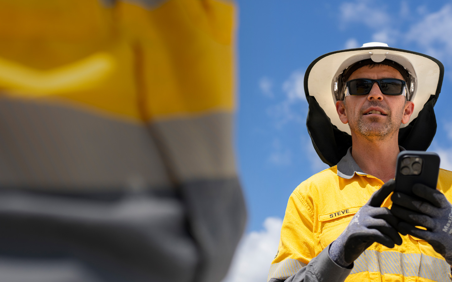 Trabalhador de construção vestido com equipamento de segurança a segurar um iPhone enquanto fala com um membro da equipa