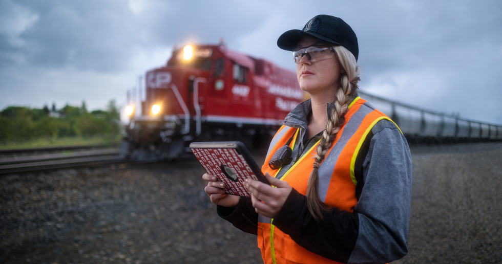 Trabalhadora ferroviária segura um iPad e verifica os carris enquanto passa um comboio