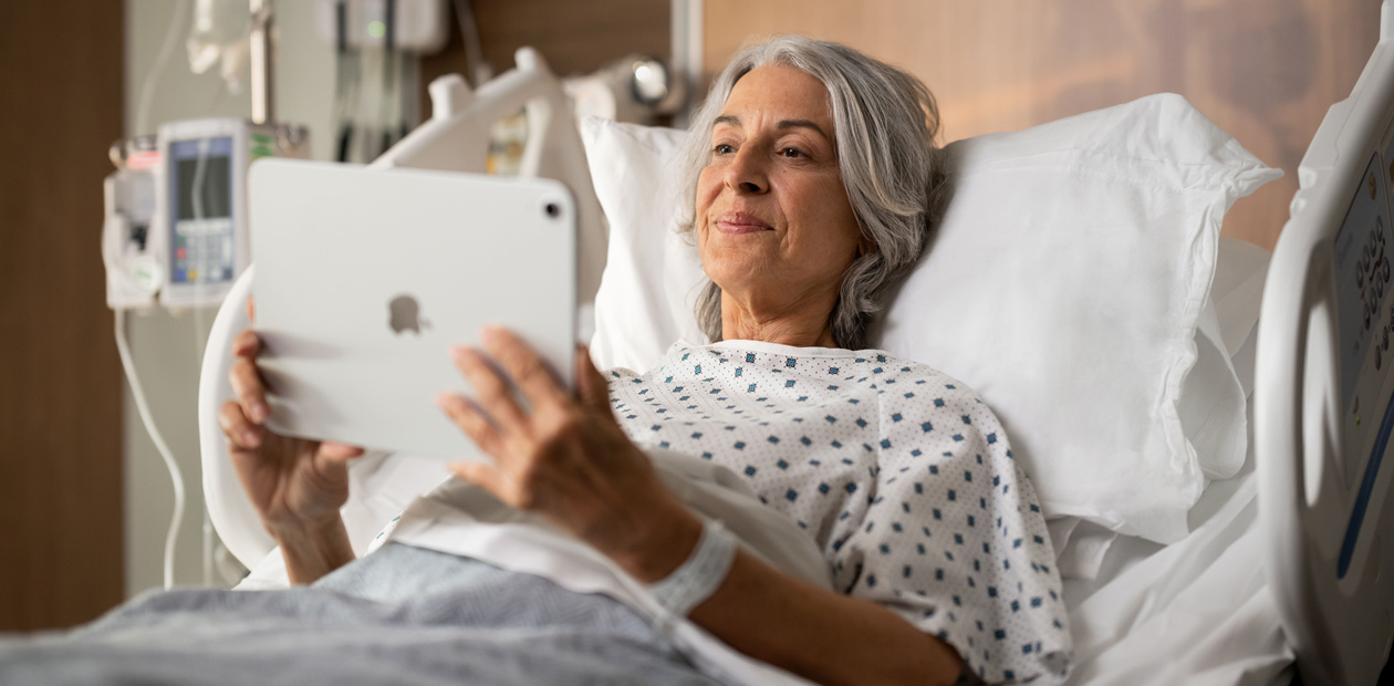 Nữ bệnh nhân nằm trên giường bệnh và nhìn vào iPad của mình.