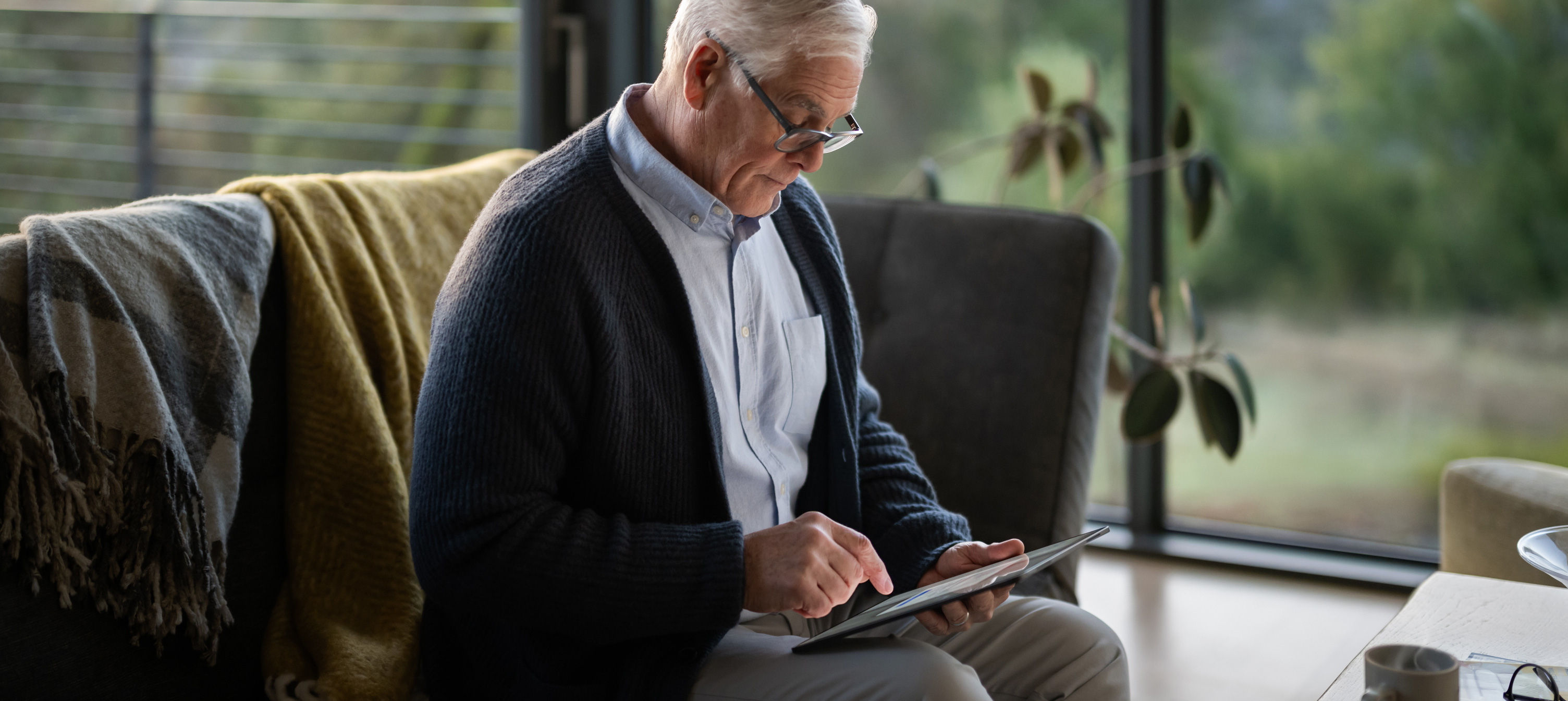 Een oudere man zit op een bank naar een iPad te kijken.