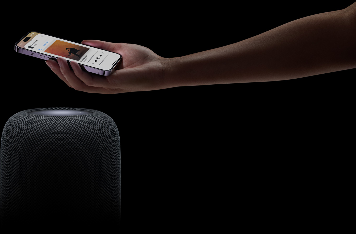 Eine Hand, die von rechts kommt, hält ein iPhone über einen HomePod Lautsprecher