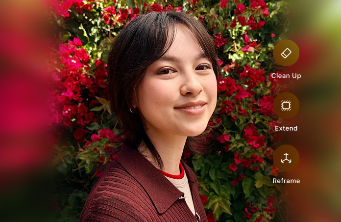 Foto de una persona sonriente de cabello marrón, vistiendo un suéter marrón, rodeada de flores rojas, demostración de edición de fotos con IA con las opciones Borrador, Ampliar y Reencuadrar en la foto