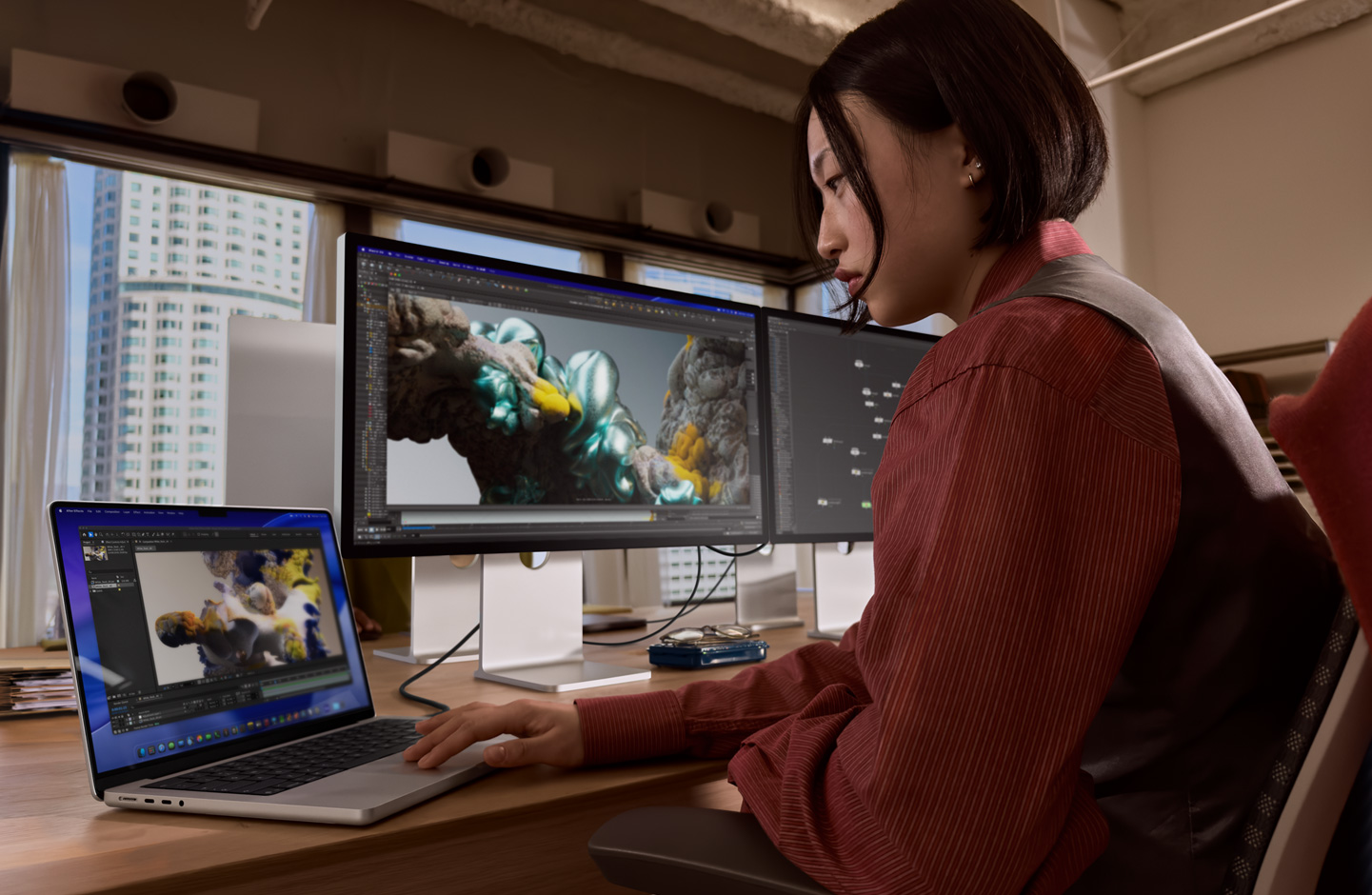 한 사람이 사무실에서 Thunderbolt 5 포트로 Studio Display XDR에 연결된 MacBook 노트북으로 작업 중인 모습